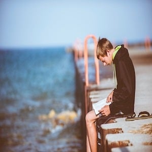 Teen reading a book on a dock by a river
