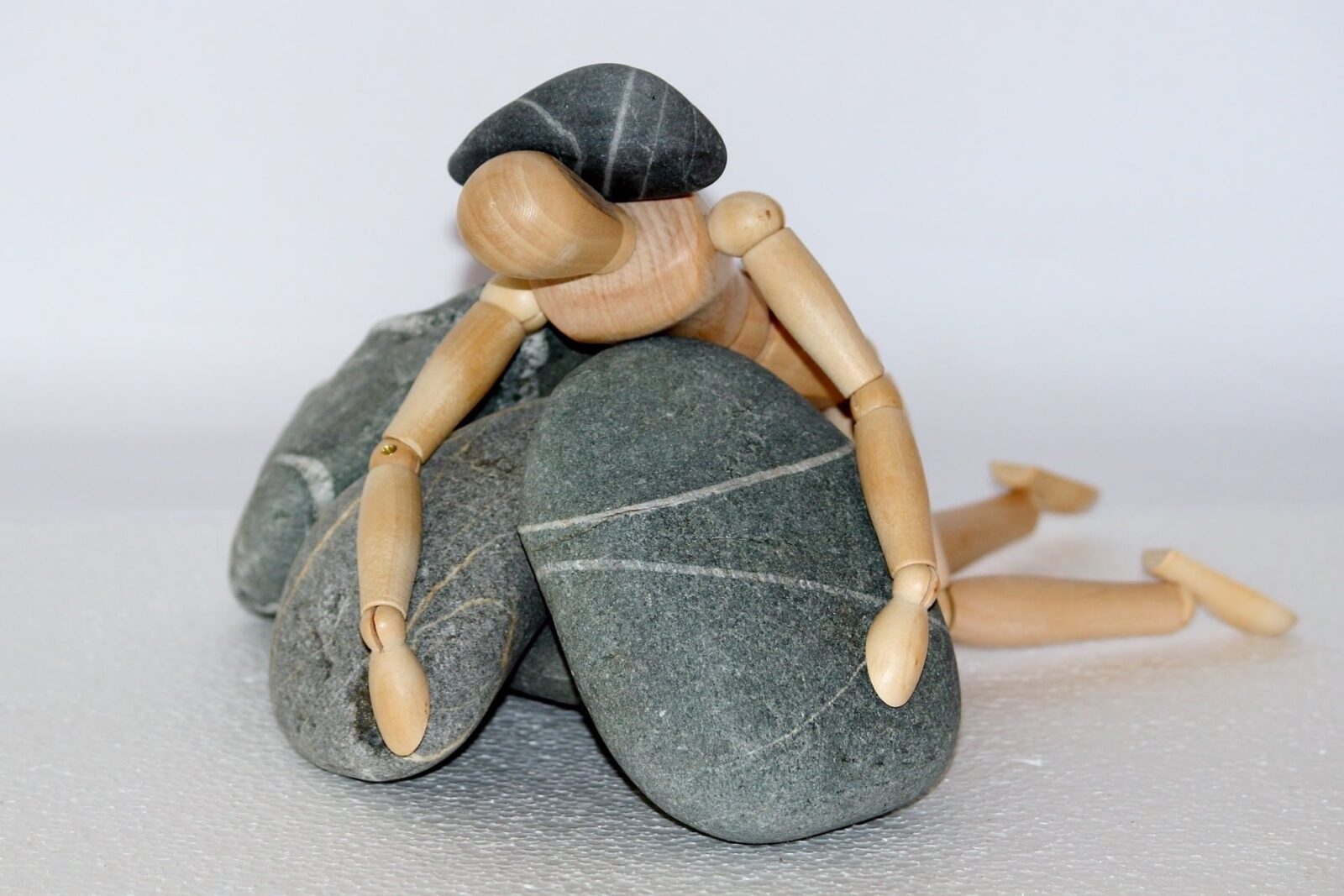 Wooden figure embracing smooth stones, under another stone