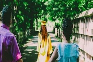 Parents watching teen walk in graduation cap and gown