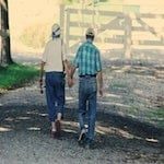 elderly couple walking away hand in hand outside on a gravel road