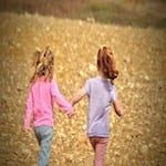 two children holding hands walking in a field