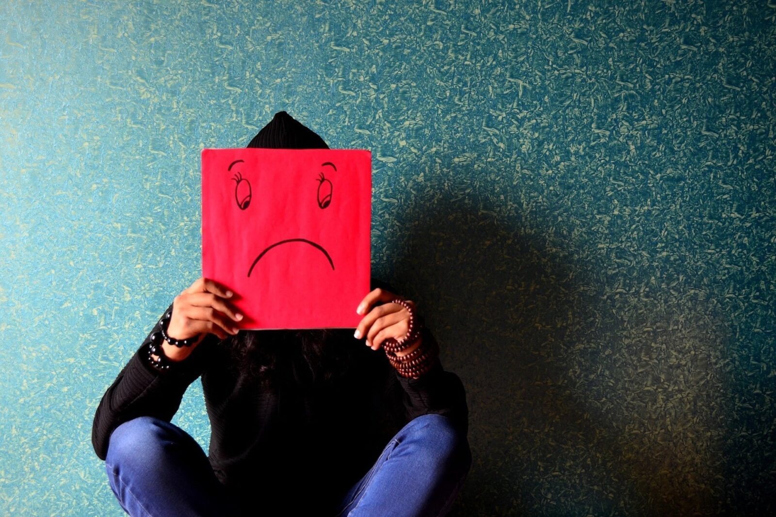 Person holding sad face poster over their face